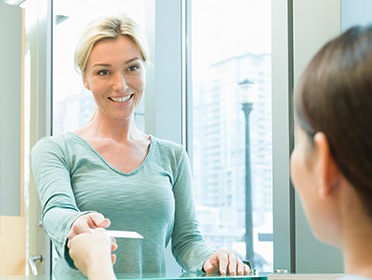 Woman giving dental team member her insurance card